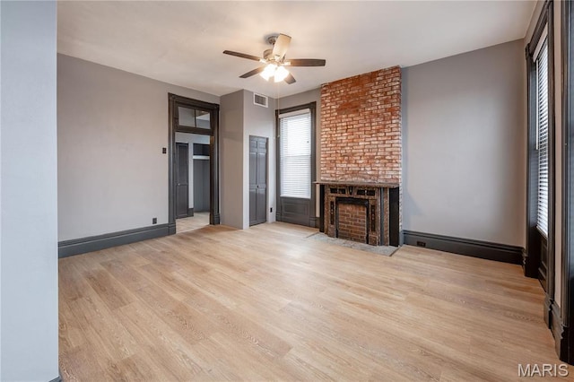 unfurnished living room with ceiling fan, light wood-style flooring, a brick fireplace, and baseboards