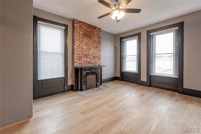 unfurnished living room featuring a ceiling fan, light wood-style flooring, and a brick fireplace