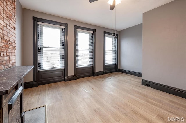 unfurnished dining area with light wood-type flooring, a ceiling fan, and baseboards