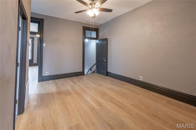 empty room with light wood-style floors, a ceiling fan, and baseboards
