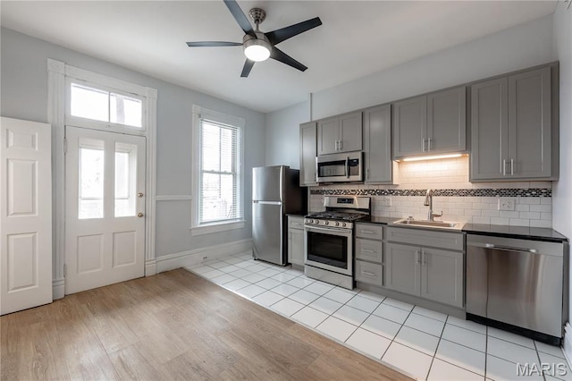 kitchen featuring appliances with stainless steel finishes, a sink, gray cabinets, and tasteful backsplash