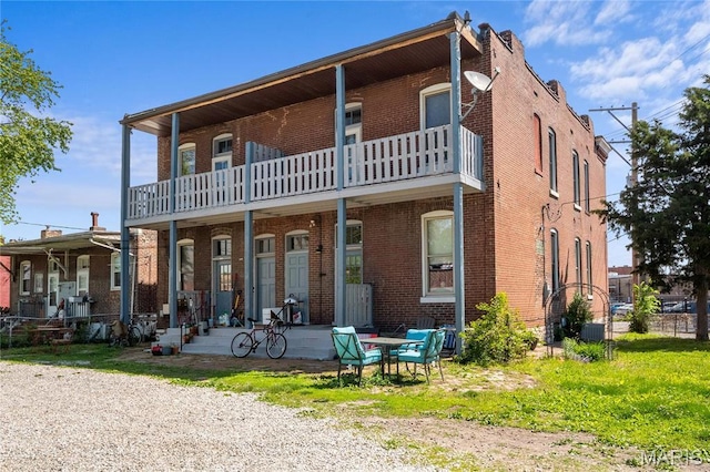 back of house featuring brick siding and a balcony