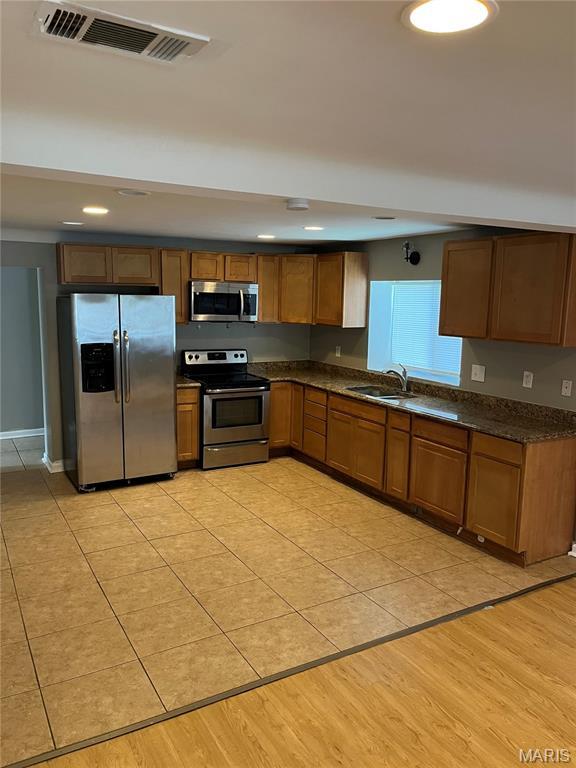 3253 Coles Ave, Saint Louis, MO 63114 - kitchen with stainless steel appliances, dark countertops, a sink, light tile patterned floors, and brown cabinetry