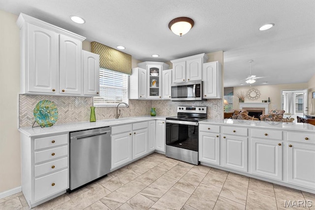 kitchen featuring stainless steel appliances, a sink, a ceiling fan, glass insert cabinets, and a fireplace