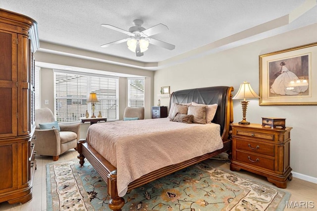 bedroom with a textured ceiling, ceiling fan, baseboards, light wood-style flooring, and a tray ceiling