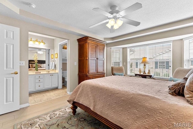 bedroom with light wood finished floors, ensuite bathroom, a textured ceiling, and a ceiling fan