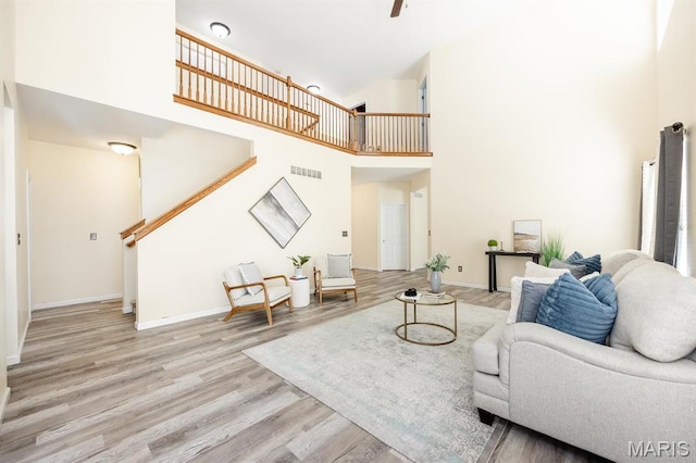 living room featuring a towering ceiling, stairs, wood finished floors, and baseboards