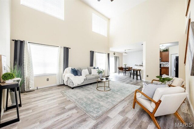 living room with a towering ceiling, plenty of natural light, light wood-type flooring, and baseboards