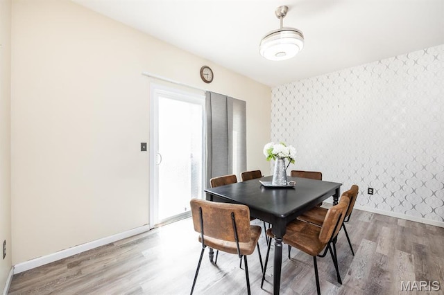 dining room featuring an accent wall, wallpapered walls, light wood-type flooring, and baseboards
