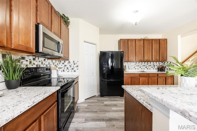 kitchen with black appliances, light wood-style floors, brown cabinets, and tasteful backsplash
