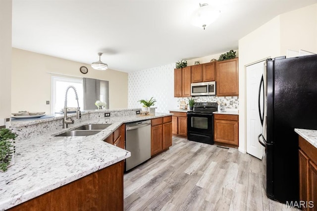 kitchen with black appliances, a sink, brown cabinetry, and light wood finished floors