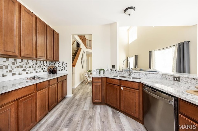 kitchen with stainless steel dishwasher, a sink, light stone counters, light wood-style floors, and tasteful backsplash