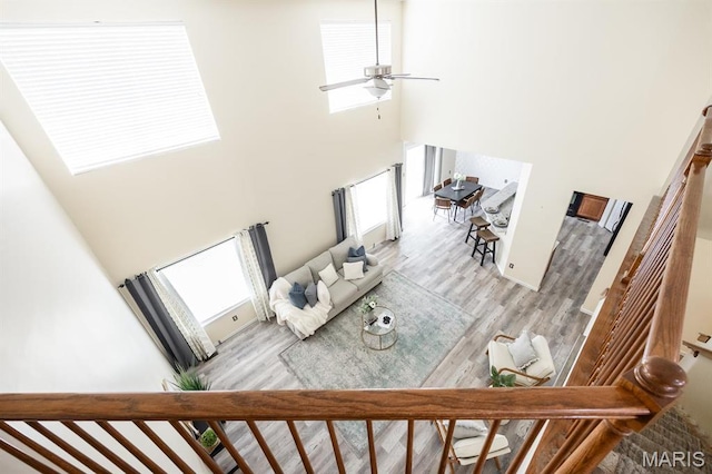 living room with a high ceiling, wood finished floors, ceiling fan, and stairs