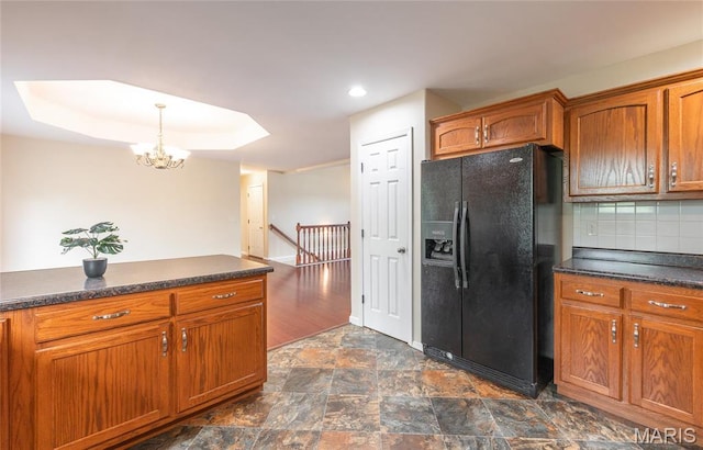 19252 Lambert Ln, Waynesville, MO 65583 - kitchen with black fridge, a chandelier, dark countertops, tasteful backsplash, and brown cabinets