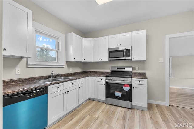 kitchen with appliances with stainless steel finishes, a sink, light wood finished floors, and dark countertops