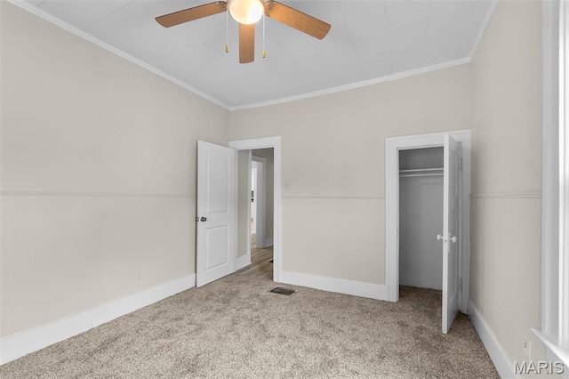 unfurnished bedroom with crown molding, carpet, a closet, baseboards, and ceiling fan
