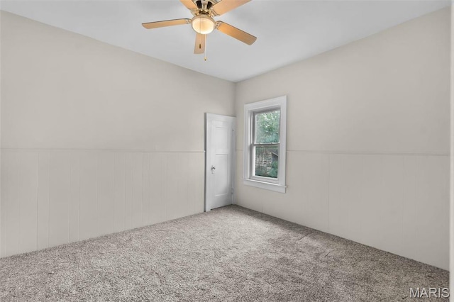 empty room with carpet floors, a ceiling fan, and a wainscoted wall