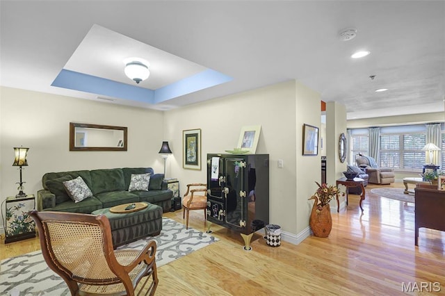 living room featuring light wood-type flooring, baseboards, recessed lighting, and a raised ceiling