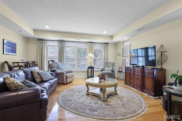 living area with a tray ceiling, light wood-type flooring, recessed lighting, and baseboards