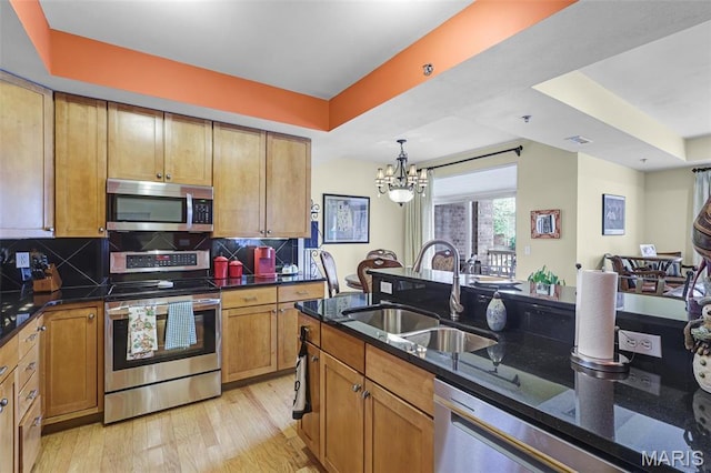 kitchen with stainless steel appliances, a sink, a chandelier, light wood finished floors, and dark stone countertops