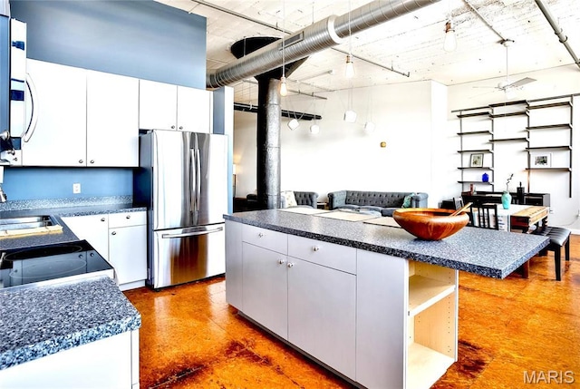 kitchen featuring freestanding refrigerator, dark countertops, a center island, and a sink