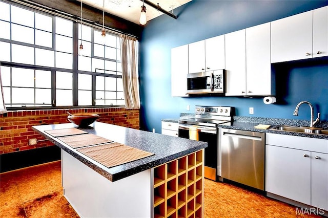 kitchen featuring appliances with stainless steel finishes, a sink, dark countertops, brick wall, and white cabinets