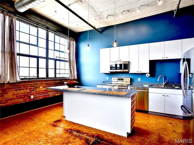 kitchen with stainless steel appliances, dark countertops, track lighting, a sink, and white cabinets