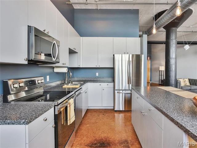 kitchen featuring appliances with stainless steel finishes, dark countertops, a sink, and white cabinets