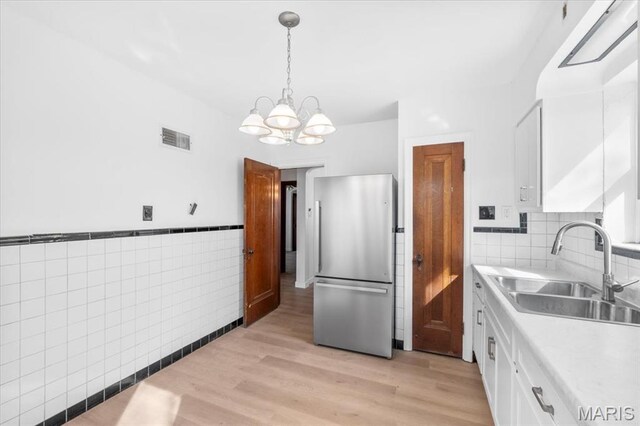 5034 Queens Ave, Saint Louis, MO 63115 - kitchen featuring freestanding refrigerator, a sink, a chandelier, white cabinetry, and tile walls