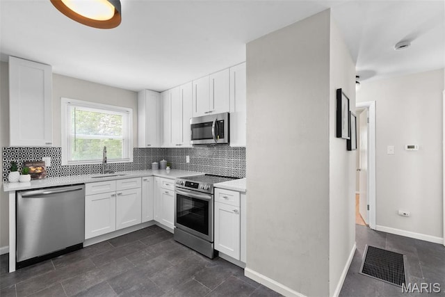 kitchen with appliances with stainless steel finishes, a sink, backsplash, light countertops, and white cabinets