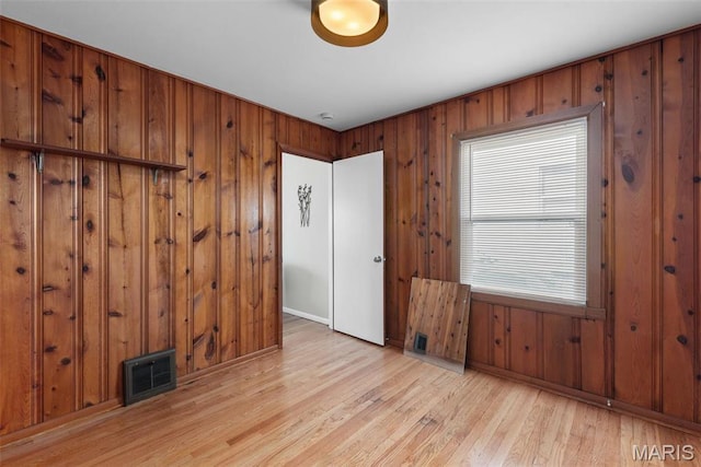unfurnished room featuring light wood finished floors, wooden walls, baseboards, and a smoke detector
