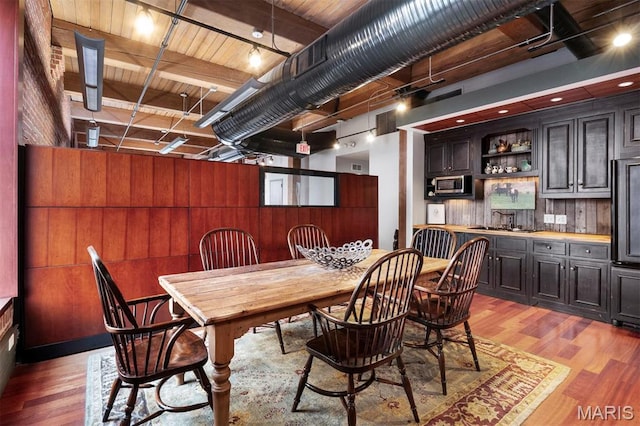 dining room featuring light wood-style flooring, bar area, and wood walls