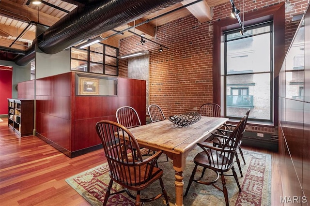 dining space with brick wall, wood finished floors, and track lighting