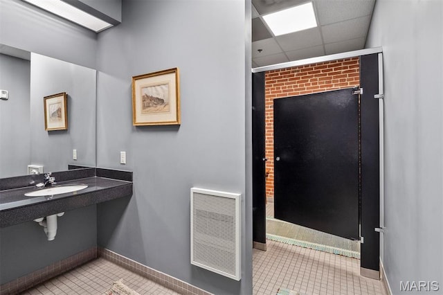 bathroom with a sink, tile patterned floors, baseboards, and a paneled ceiling
