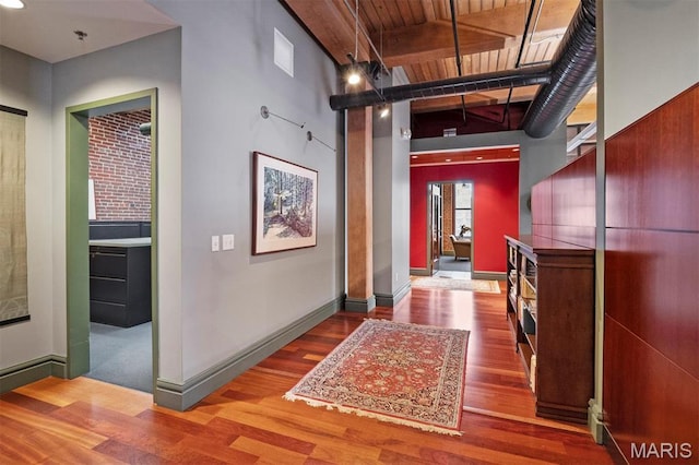 corridor featuring wood finished floors, beam ceiling, baseboards, and wooden ceiling