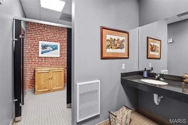 bathroom with a drop ceiling, baseboards, a sink, and tile patterned flooring
