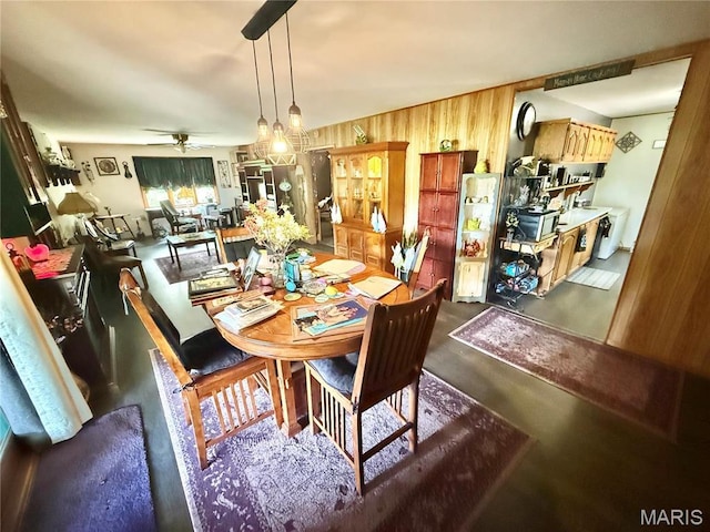 dining room with a ceiling fan, wood walls, and concrete flooring