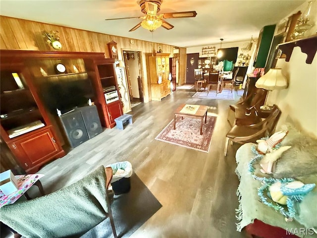 living area with ceiling fan, wooden walls, and wood finished floors