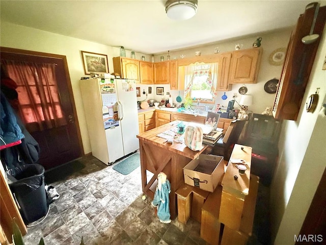 kitchen featuring freestanding refrigerator, light brown cabinets, a sink, light countertops, and stone finish floors