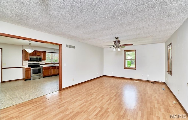 unfurnished living room with light wood-style flooring, healthy amount of natural light, a ceiling fan, and a textured ceiling