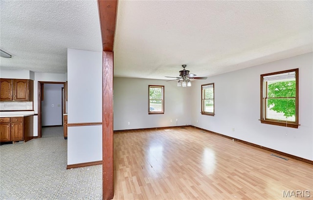 unfurnished living room featuring a textured ceiling, ceiling fan, light wood-style flooring, and baseboards