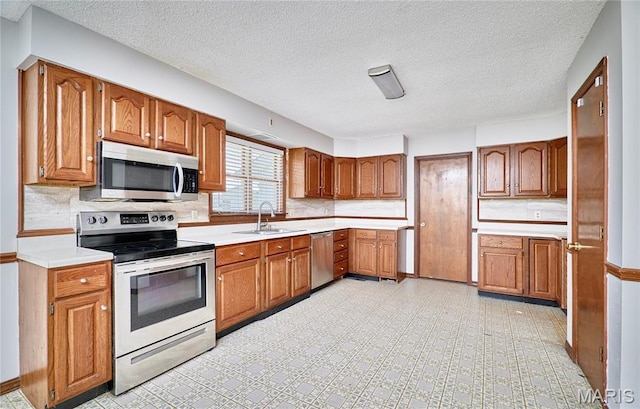 kitchen with stainless steel appliances, brown cabinetry, light countertops, and a textured ceiling