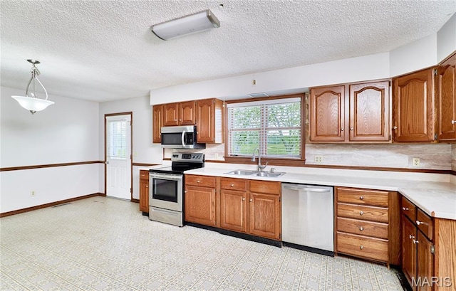 kitchen featuring stainless steel appliances, a sink, healthy amount of natural light, brown cabinets, and a textured ceiling