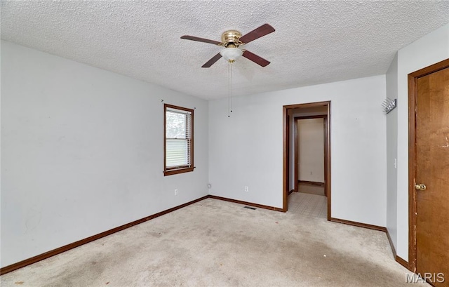 empty room with a ceiling fan, light colored carpet, baseboards, and a textured ceiling