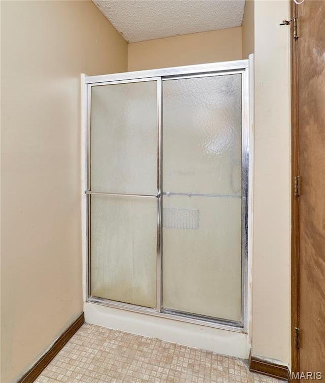 bathroom featuring a shower with door, a textured ceiling, and baseboards