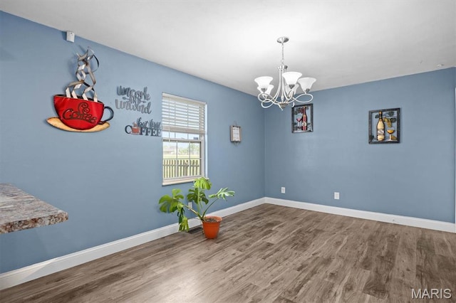 spare room with a chandelier, wood finished floors, and baseboards