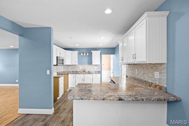 kitchen with stainless steel microwave, a peninsula, wood finished floors, baseboards, and tasteful backsplash