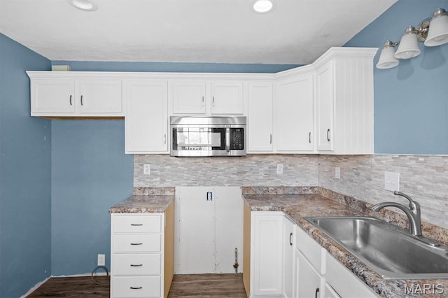kitchen with stainless steel microwave, a sink, dark wood-type flooring, white cabinetry, and tasteful backsplash