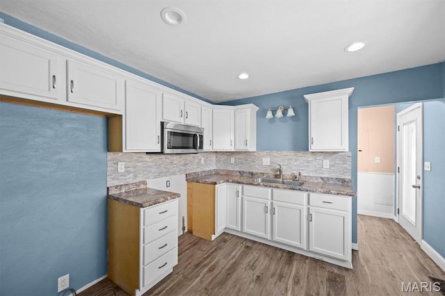 kitchen featuring stainless steel microwave, a sink, wood finished floors, decorative backsplash, and white cabinetry