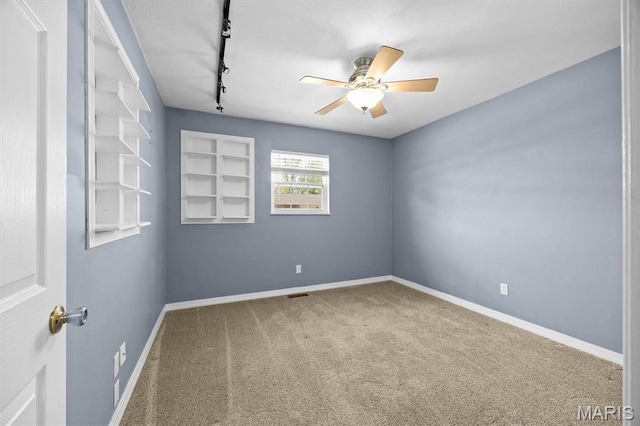 carpeted empty room with a ceiling fan, baseboards, and rail lighting